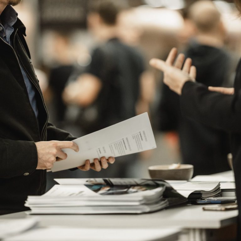 Zwei Personen, die an einem Stand stehen und sich überhalten mit Werbematerial