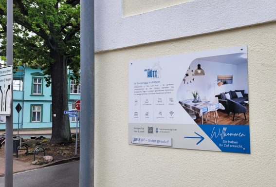 Informationsschild an einer Wand mit einem Wegweiser und Bildern eines Innenraums.